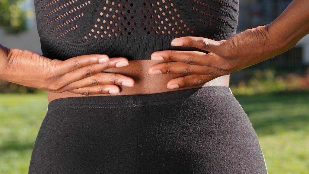Close-up of a woman's hands gripping her painful back while outdoors.